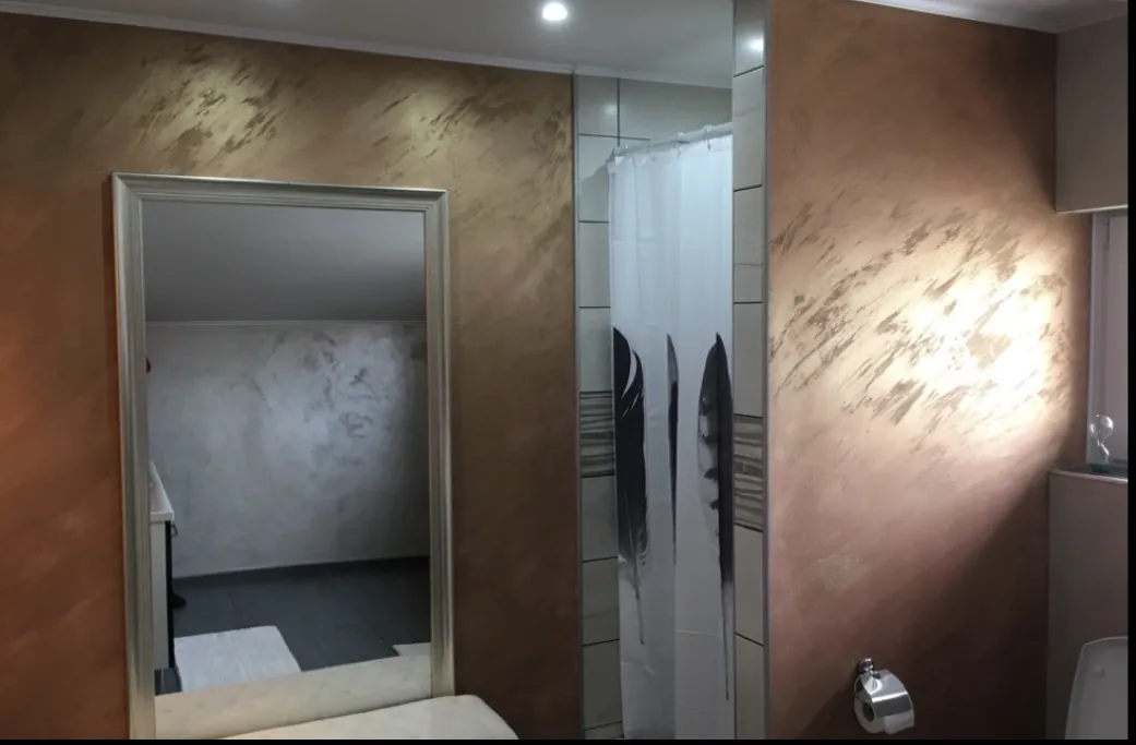 Badezimmer mit dekorativ gespachtelten Wandflächen in einem metallischen Kupferton.